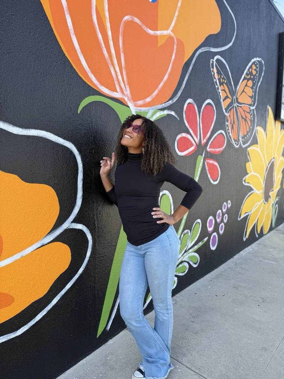 Cheyenne Scott standing in front of her colorful floral mural at All Floors 4 Less